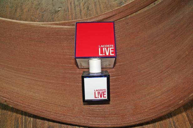 Eine Flasche Lacoste L!VE Parfüm steht auf einer Holzschale.