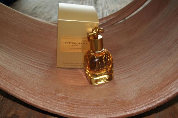 Eine Flasche „Bottega Veneta Knot“ Eau de Parfum steht vor der goldenen Verpackung.