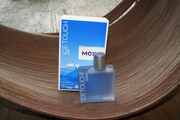 Ein Flakon und die Verpackung von „Ice Touch Man“ der Marke Mexx stehen auf einer Holzschale.