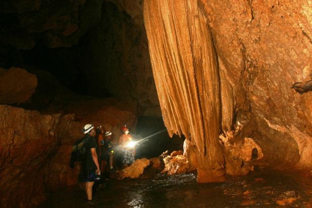 Eine Gruppe von Menschen erkundet eine Höhle mit Stalaktiten und Wasser.