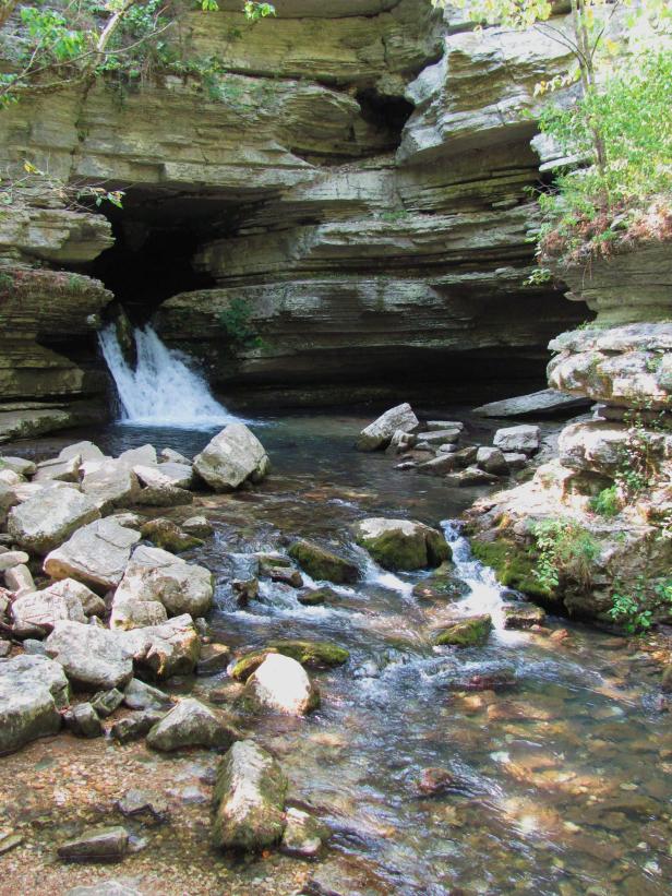 Ein kleiner Wasserfall fließt aus einer Höhle in einen Bach.