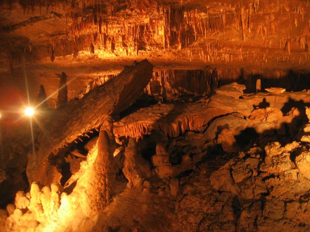 Innenansicht einer Höhle mit Stalaktiten und Stalagmiten, beleuchtet mit warmem Licht.