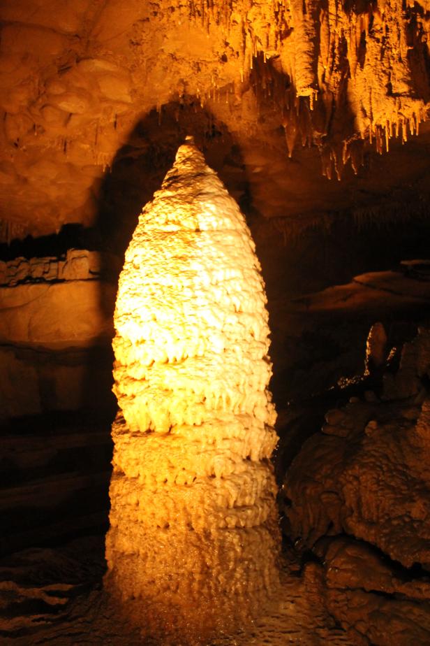 Ein großer Stalagmit in einer Höhle, beleuchtet mit warmem Licht.