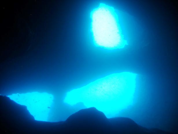 Unterwasseraufnahme von blauem Licht, das durch Öffnungen in einer Höhle scheint.