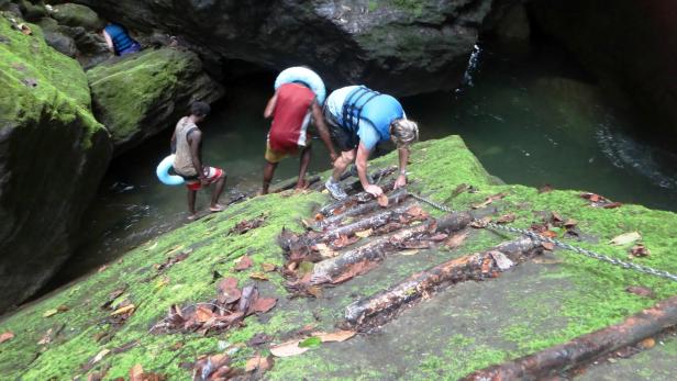 Drei Personen bereiten sich mit Schwimmreifen und Schwimmweste auf das Schwimmen in einem Fluss vor.