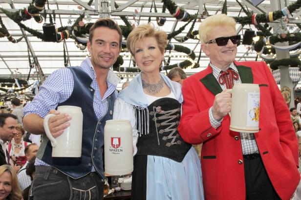 Drei Personen in Tracht halten Bierkrüge auf dem Oktoberfest.