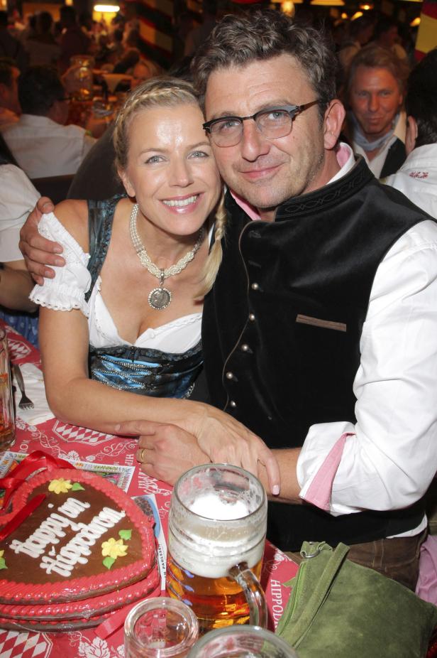 Ein Paar in Tracht posiert auf dem Oktoberfest mit Lebkuchenherz und Bierkrug.