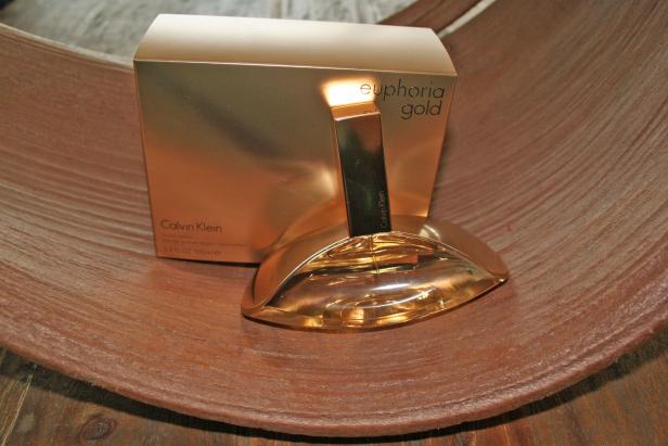 Ein goldener „Euphoria Gold“-Duft von Calvin Klein auf einer braunen Oberfläche.