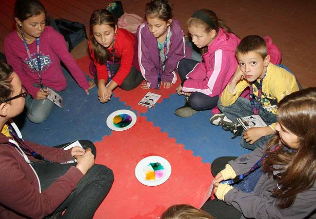Eine Gruppe Kinder sitzt im Kreis um zwei Teller mit farbigem Gel.