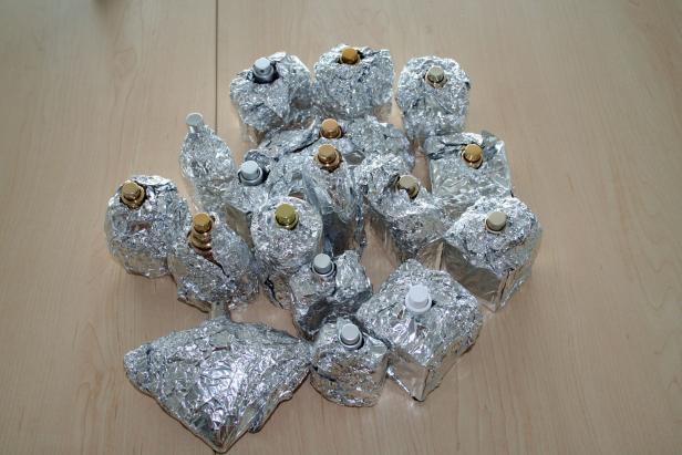 Mehrere in Alufolie eingewickelte Parfümflaschen stehen auf einem Holztisch.