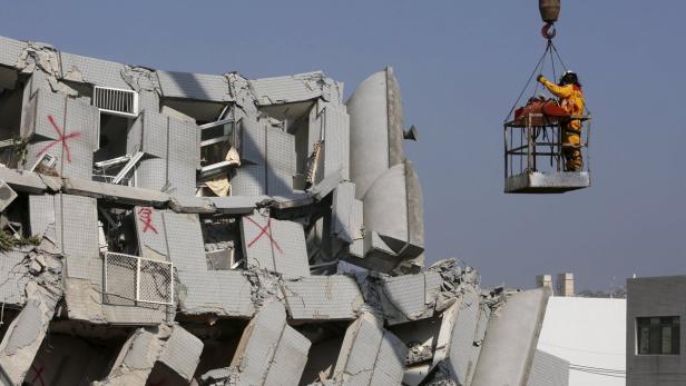 Ein Rettungsarbeiter wird mit einem Kran zu einem durch ein Erdbeben zerstörten Gebäude gehoben.