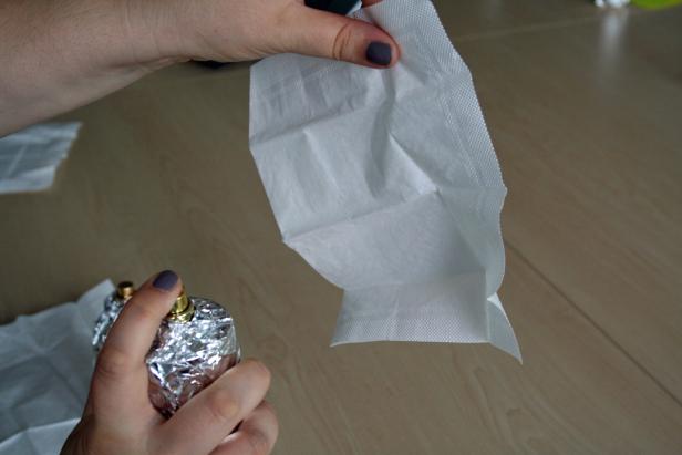 Eine Hand hält ein Parfümfläschchen, das mit Alufolie umwickelt ist, und ein Papiertaschentuch.