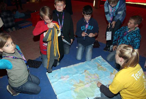 Eine Gruppe Kinder kniet um eine Weltkarte auf dem Boden.