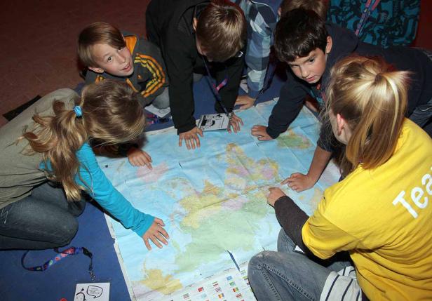 Eine Gruppe Kinder beugt sich über eine Weltkarte und zeigt auf verschiedene Orte.