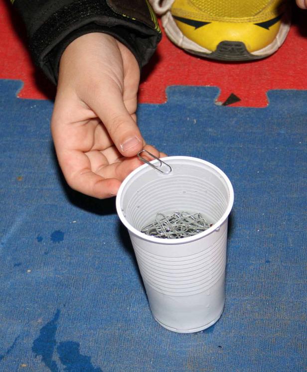 Eine Hand hält eine Büroklammer über einen Becher voller Büroklammern.