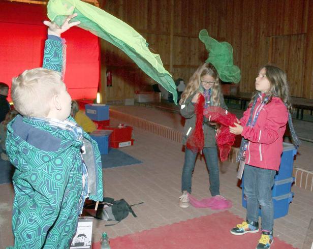 Drei Kinder spielen mit bunten Tüchern in einem Raum.