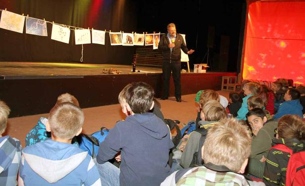 Ein Mann hält einen Vortrag vor einer Gruppe von Kindern auf einer Bühne.