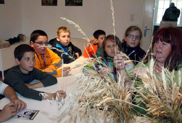 Eine Gruppe Kinder sitzt mit einer Frau an einem Tisch und betrachtet Getreideähren.