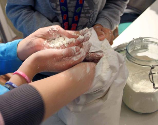 Mehrere Hände greifen in einen Sack und eine Dose mit Mehl.