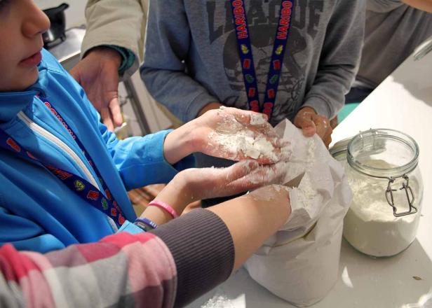 Kinderhände greifen in eine Tüte mit Mehl, umgeben von Erwachsenen.