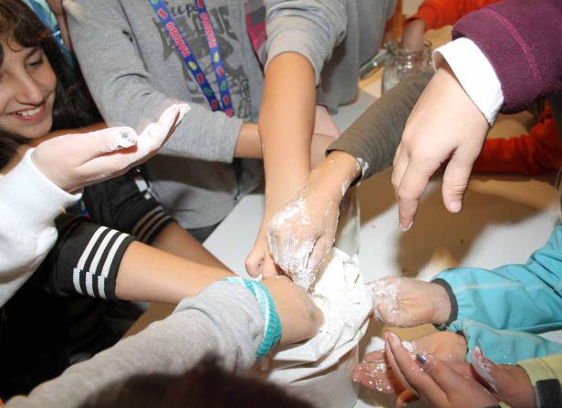 Mehrere Kinderhände greifen in eine Tüte mit Mehl.