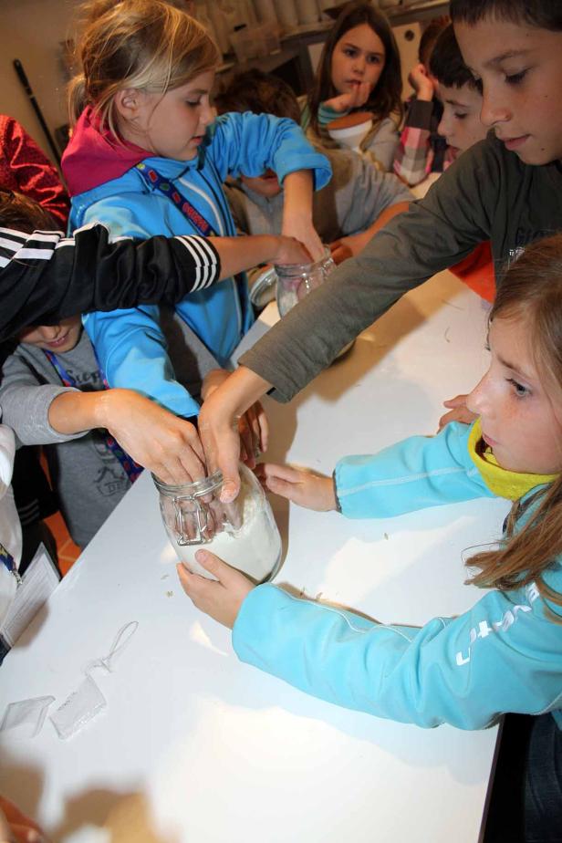 Mehrere Kinder greifen gleichzeitig in ein Glas mit einer weißen Substanz.