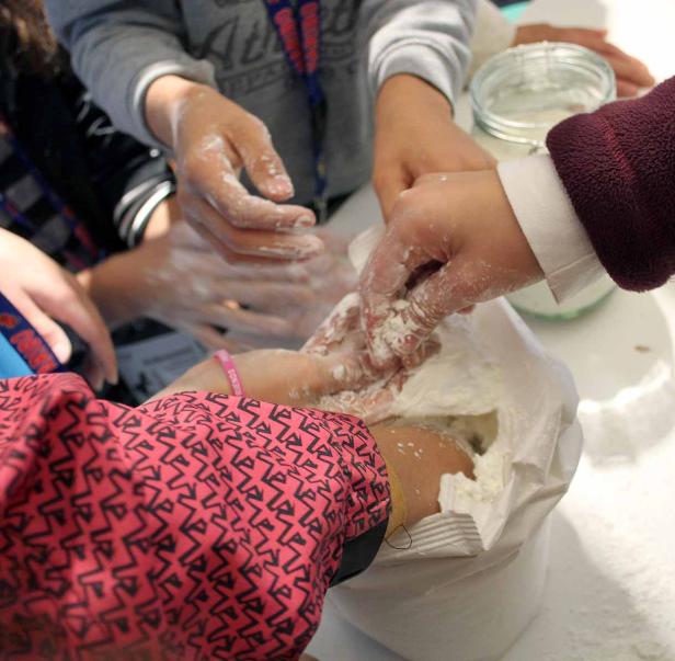 Mehrere Kinderhände greifen in eine Tüte mit Mehl.