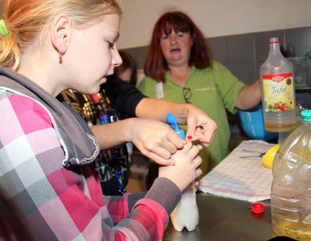 Ein Mädchen füllt eine Flüssigkeit in eine Plastikflasche, während eine Frau assistiert.