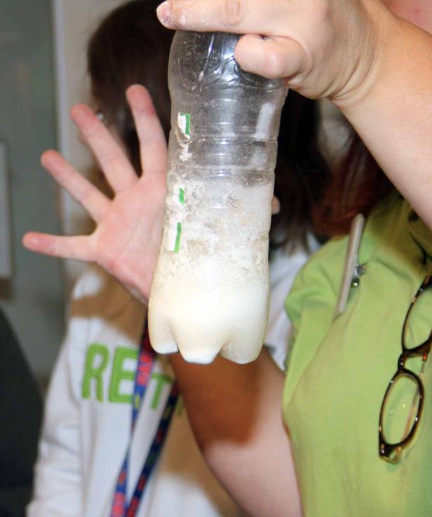 Eine Person hält eine Plastikflasche mit einer trüben, weißen Flüssigkeit hoch.
