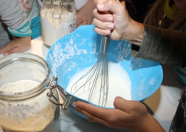 Ein Kind verrührt Teig in einer blauen Schüssel mit einem Schneebesen.