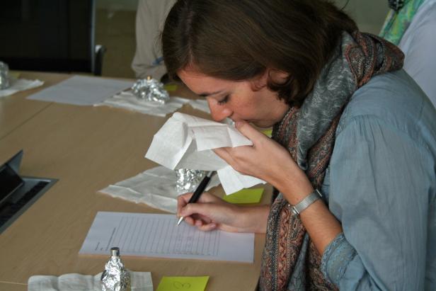 Eine Frau riecht an einem Tuch und macht Notizen auf einem Blatt Papier.