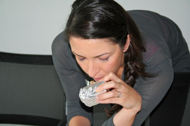 Eine Frau beugt sich vor und hält ein in Alufolie verpacktes Objekt an ihre Lippen.