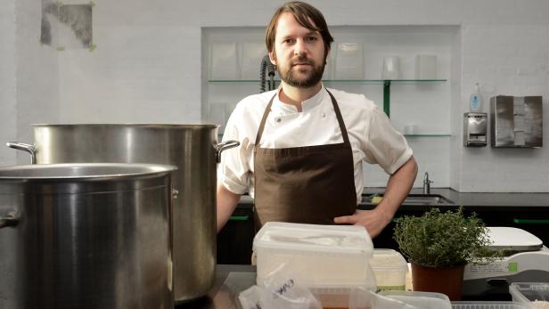 Ein Koch steht in einer Küche mit großen Töpfen und Zutaten.