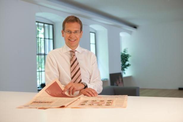 Ein Mann mit Brille und Krawatte liest eine Zeitung an einem Tisch.