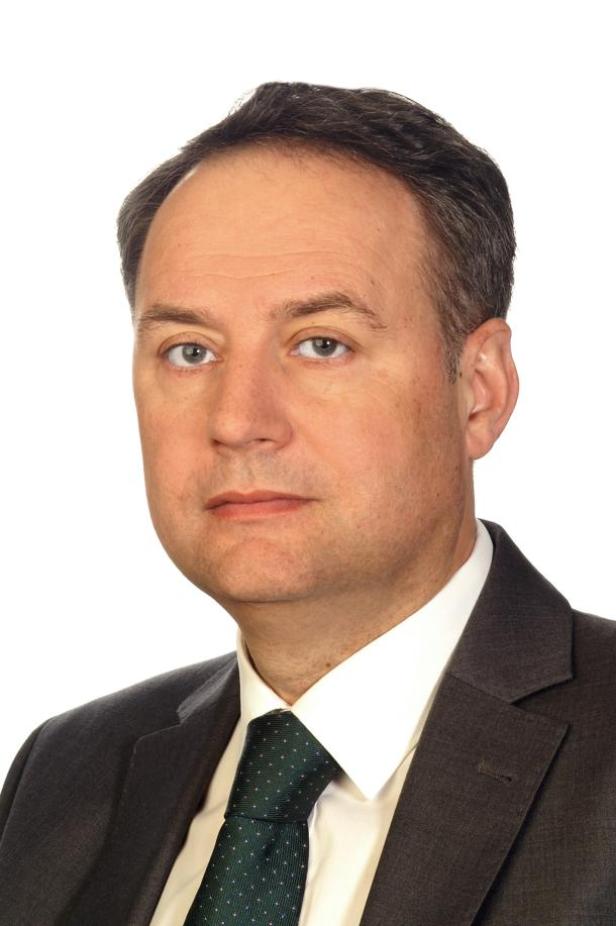 Ein Mann mit Anzug und Krawatte vor einem weißen Hintergrund.