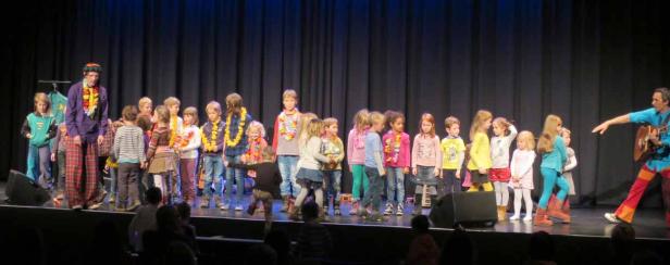 Eine Gruppe Kinder steht mit zwei Erwachsenen auf einer Bühne.