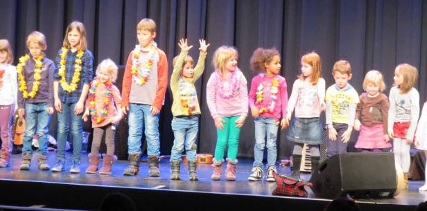 Eine Gruppe Kinder steht mit Blumenketten auf einer Bühne.