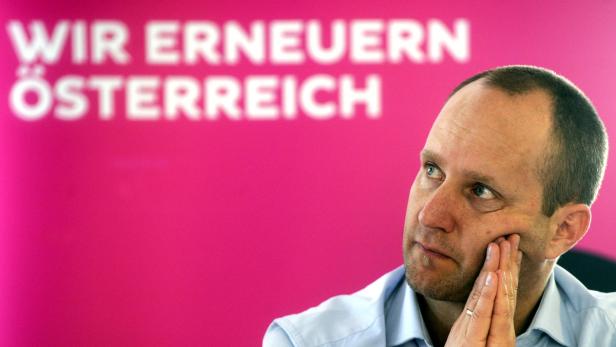 Ein Mann hält seine Hand ans Gesicht vor einem pinkfarbenen Hintergrund mit dem Text „Wir erneuern Österreich“.