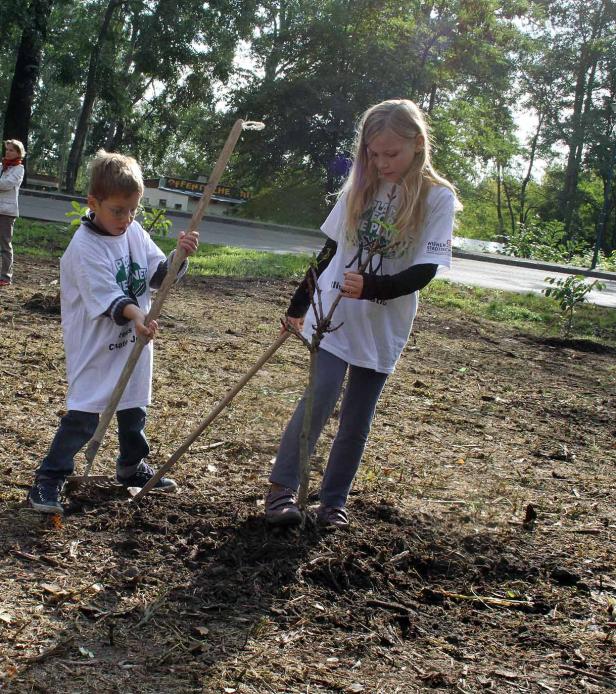 Zwei Kinder pflanzen einen Baum mit Hilfe von Stöcken.