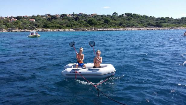Zwei Jungen sitzen in einem Schlauchboot auf dem Meer und halten Fischernetze hoch.