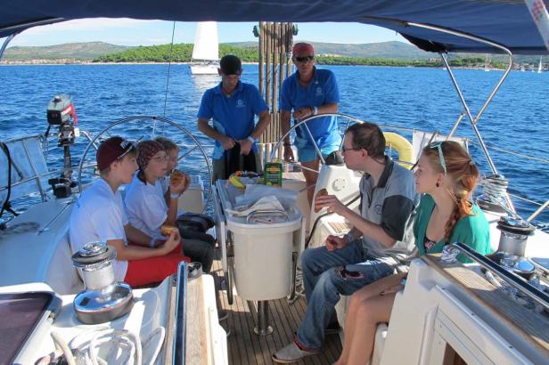 Eine Gruppe von Menschen genießt eine Mahlzeit auf einem Segelboot auf dem Meer.