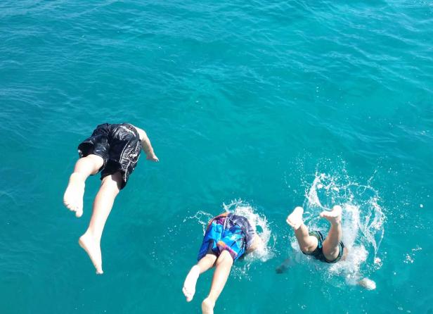 Drei Personen springen kopfüber in türkisfarbenes Wasser.