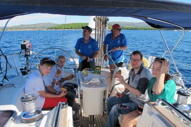 Eine Gruppe von Menschen genießt Croissants auf einem Segelboot auf dem Meer.