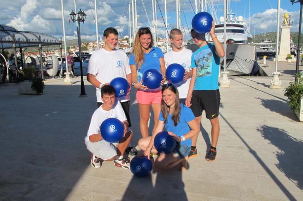 Eine Gruppe von Jugendlichen posiert mit blauen Bällen in einem Hafen.