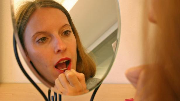 Eine Frau trägt Lippenstift vor einem Spiegel auf.