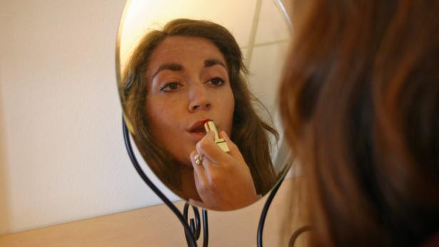 Eine Frau trägt Lippenstift vor einem Spiegel auf.