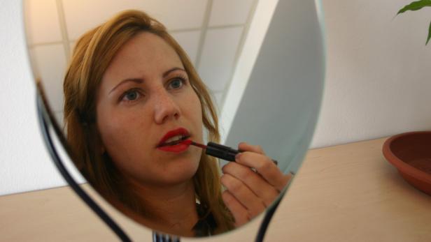 Eine Frau trägt roten Lippenstift vor einem Spiegel auf.