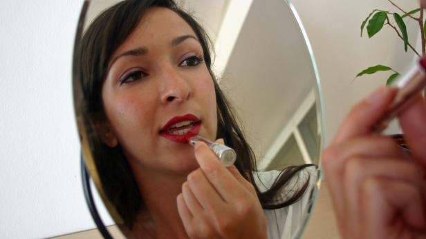 Eine Frau trägt roten Lippenstift vor einem Spiegel auf.