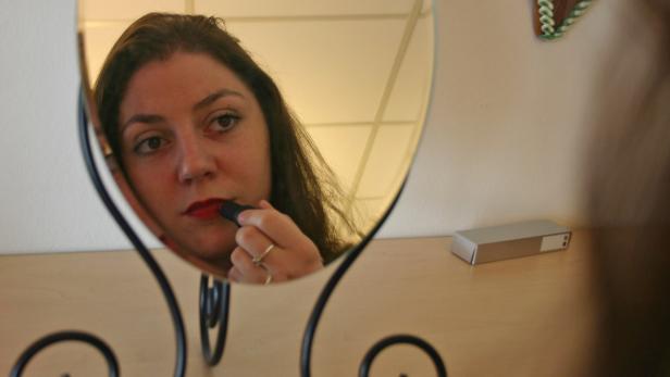 Eine Frau trägt Lippenstift auf, während sie in einen Spiegel schaut.