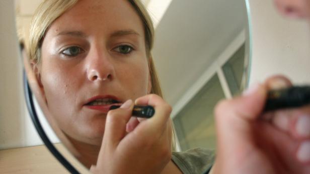 Eine Frau trägt Lippenstift vor einem Spiegel auf.